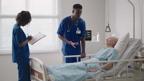 Dos-Médicos-Negros-Están-Hablando-Con-Un-Paciente-Acostado-En-Una-Habitación-De-Hospital